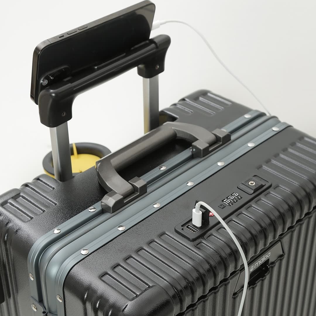 Topo de uma mala Su&eacute;cia preta, com um celular apoiado na al&ccedil;a retr&aacute;til, ligado por cabo, e um copo no porta-copos